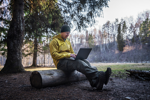 Joyful man using laptop at the campfire in the woods