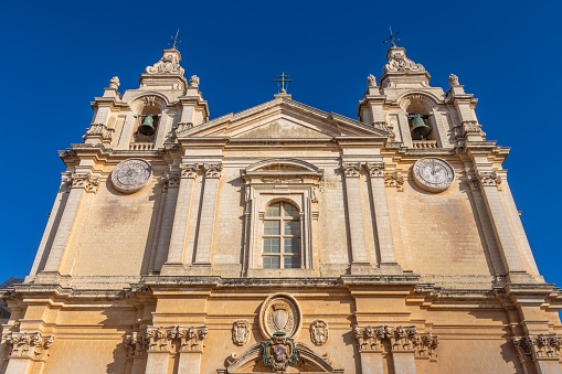 A stunning, ornate church building boasting two clocks atop its facade in Mdina Old City Fortress