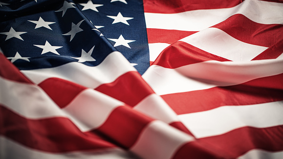 Close up of Christian cross pin with American flag colors is pinned on blue jeans jacket. Patriotism and religious rights concept