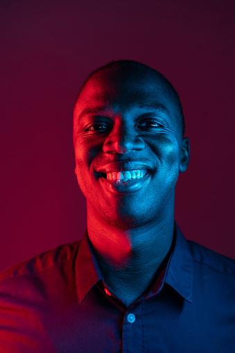 An African-American man is smiling at the camera, wearing a smart shirt against a dark purple background