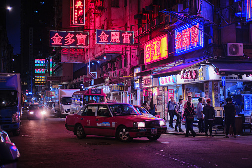 Mong Kok, Hong Kong - April 12 2023: A Traditional red Taxi and colorful neon light signs