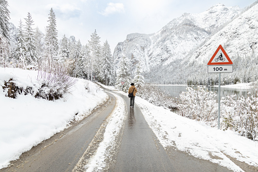 Beautiful view of a male tourist walking on road by Toblacher See (Dobbiaco Lake) in a snowy winter day; Dolomites, Bolzano, Italy
