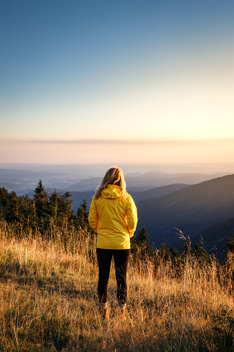 Hiker with yellow jacket relax at mountain range during sunset. Hiking in mountains