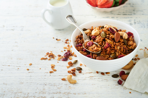 Homemade granola in glass jar with greek yogurt or milk and cashews, almonds, pumpkin with dried cranberry seeds in on white rustic wooden table background. Healthy energy breakfast or snack. Top view