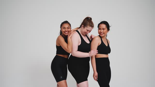 Three laughing girls in black tracksuits hugging and looking to side