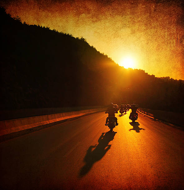 People on motorcycles at sunset A large group of motorcycles are riding into the summer sunset.  The sun is ahead of them on top of a hill and the sun rays are shining onto the motorcycles and the road.  The sky is orange, as well as the road because if the sun reflection. biker stock pictures, royalty-free photos & images