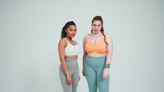 Two handsome multinational girls in sportswear posing at camera