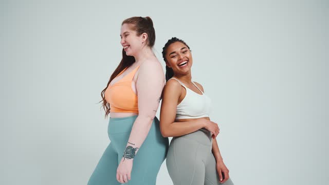 Two laughing multinational girls in sportswear standing back to back