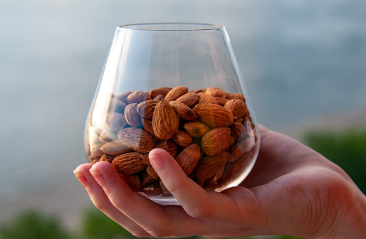 A woman's hand holds a glass with almonds on the background of a beautiful landscape with a river