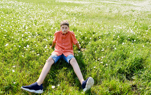 Teen boy sit on the green meadow. Teen in sunglasses. Teen looking in camera