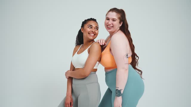 Two cheerful multinational girls in sportswear posing at camera