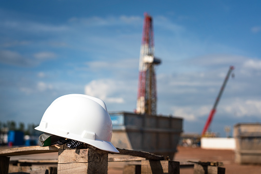 An oilfield worker safety hardhat or helmet is placed at onshore drilling rig site with blurred background of derrick structure. Ready to working in challenge industrial concept. Selective focus.