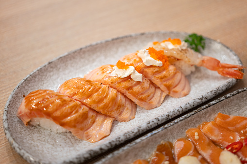 Salmon burned sushi pieces is variuos topping are served on ceramic dish and placed on wooden table. Japanese food object photo. Selective focus.