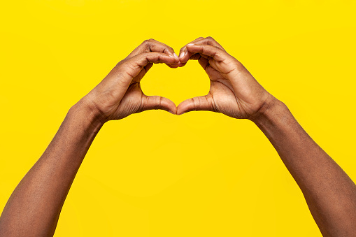 gesture of love, hands of african american man show heart on yellow isolated background, guy makes symbol of romance with his hands, close-up