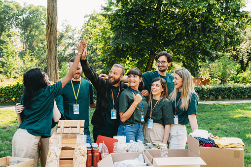 A group of volunteers are celebrating together behind the food and clothes bank table. Teamwork of volunteers working in an humanitarian aid project.