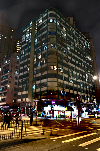 People crossing King's road at night by a corner building in North Point, Hong Kong.