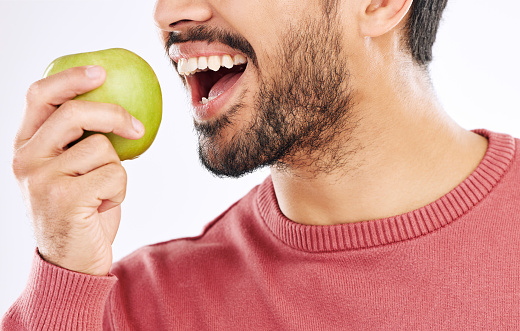 Hand, apple and man in studio for diet, nutrition and weight loss with healthy breakfast on white background. Fruit, snack and male nutritionist eating organic, clean and fiber detox routine isolated