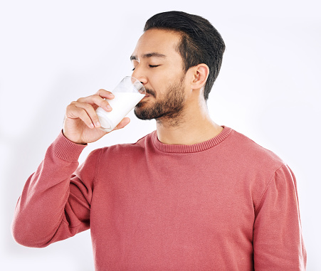 Man drinking glass of milk in studio, white background and backdrop for healthy food, smoothies and diet. Male model, food and calcium of smoothie, vanilla milkshake and nutrition of protein drink
