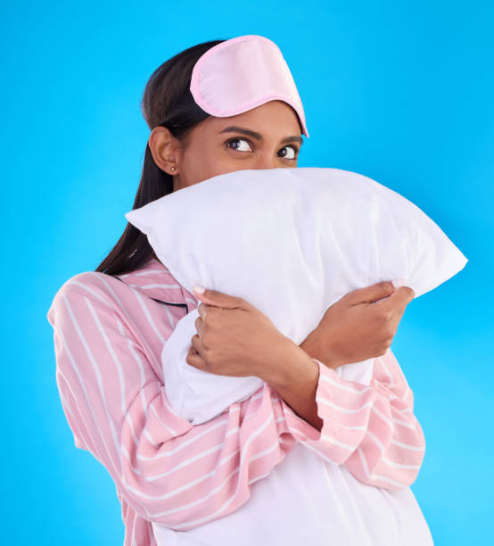 istock Comfy, bedtime and a woman hugging a pillow isolated on a blue background in a studio. Relax, rest and an Indian girl ready for sleep, napping or night rest and thinking of sleeping on a backdrop 1498172554