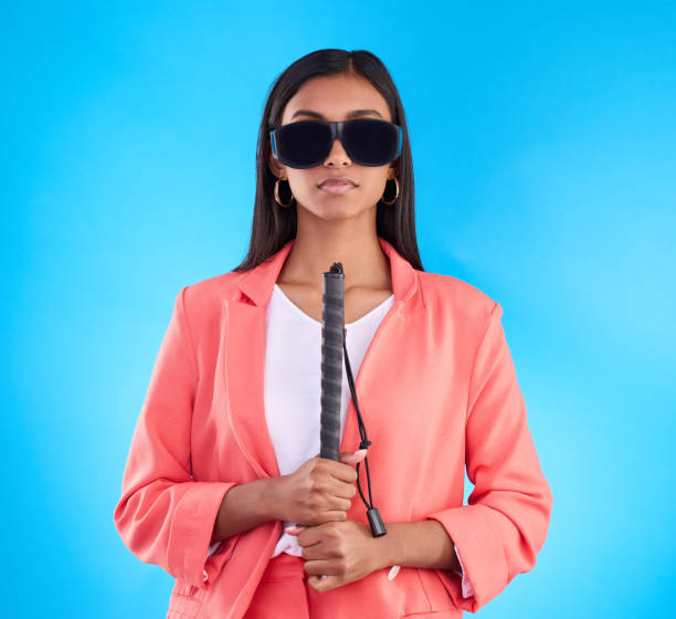 istock Blind, face and woman with disability in a studio with guide cane for eyes impairment help. Glasses, serious or young female person in post eye surgery on isolated blue background with vision problem 1498172607