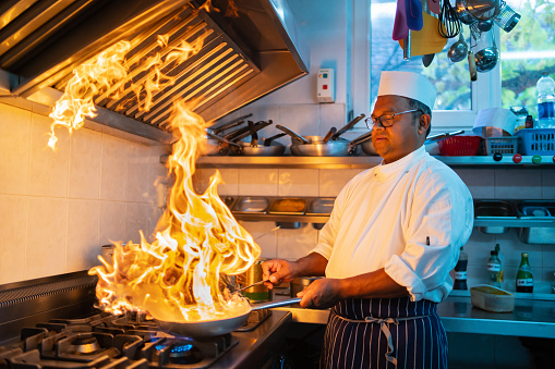 Frying off food and flaming it in a professional Indian kitchen, the chef is careful to stand well back from the spectacular flames coming off the frying pan