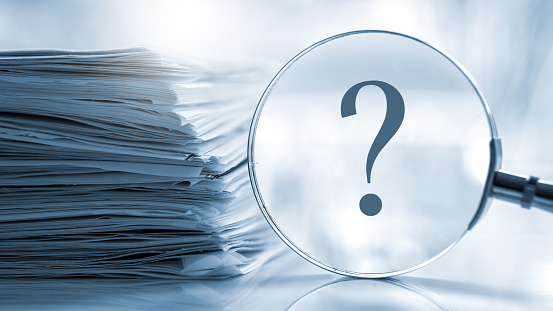 Magnifying glass with a question mark and untidy pile of documents