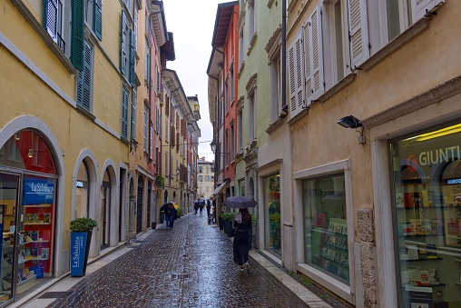 Sirmione, Italy – April 24, 2022: A group of people walking in a downtown area on a rainy day with shops and buildings on the street