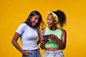 Couple of young student girls happily surprised pointing and looking at cell phone posing isolated.