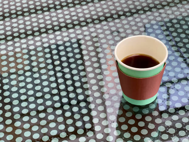 A disposable cup of beverage stands on a wet glass table