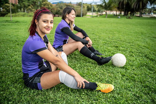 Portrait of a soccer player young woman sitting on ground outdoors