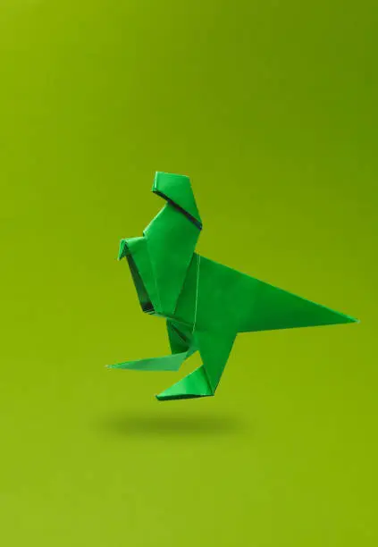 Photo of Origami dinosaur levitating on a green background