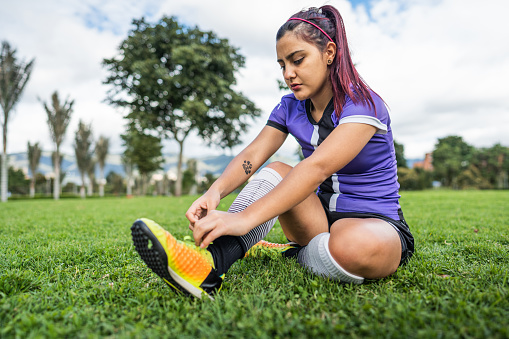Soccer player young woman tying shoe laces on soccer field