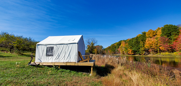 This is a photograph taken on a mobile phone outdoors of a glamping tent campsite set up by a pond with autumn colored leaves during October in the Hudson Valley area of Upstate New York.