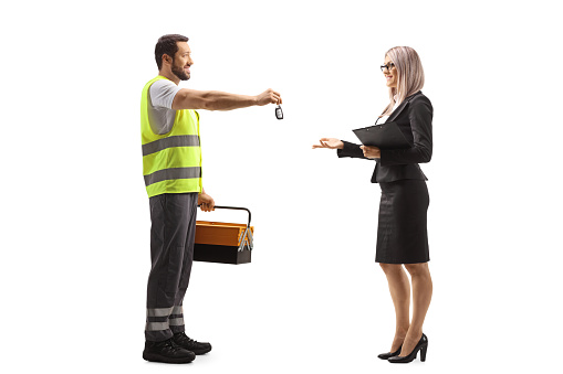 Full length profile shot of a road assistance agent in a reflective vest giving a car key to a woman isolated on white background