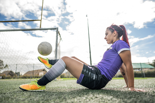 Soccer player young woman sitting juggling ball on soccer field