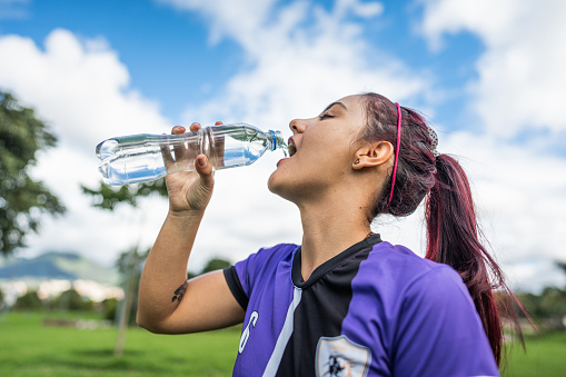 Soccer player young woman drinking water outdoors