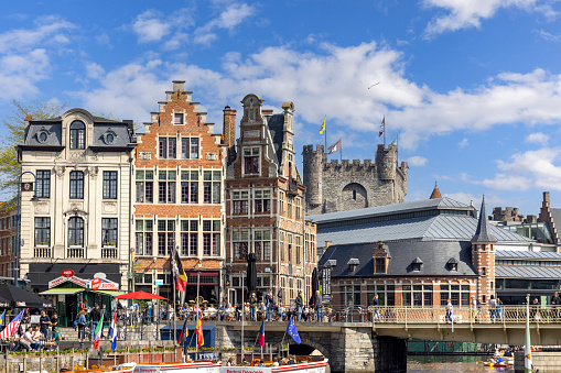 Ghent, Belgium - May 19, 2023: View of Grasbrug bridge over Lys river (Leie), colorful houses and cruise ships on the water. Gravensteen castle in the distance