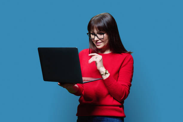 istock Friendly mature woman using laptop, over blue background 1498201759