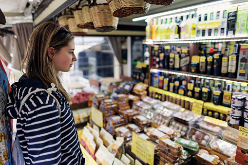 Teenage girl browsing local traditional food in a small Italian grocery store\nOvercast, rainy off-season day.\nShot with Canon R5