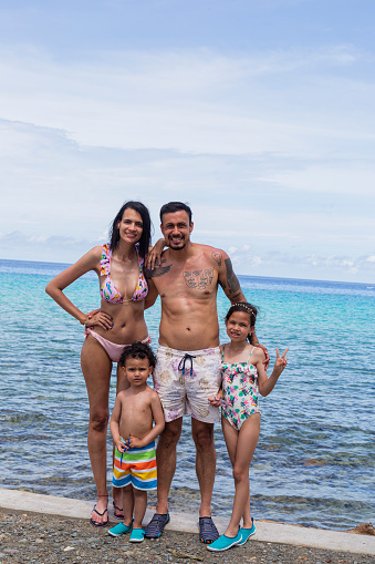 Beautiful photograph of a traditional Latino family with two beautiful children dressed in sea clothes looking towards the camera that portrays them showing their happiness to be on the beautiful island of San Andres