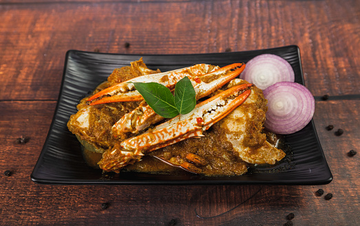 Spicy and delicious crab roast on a wooden table. Stir Fried Crab with Curry Powder garnished with onion, curry leaves and black pepper. Seafood Style.