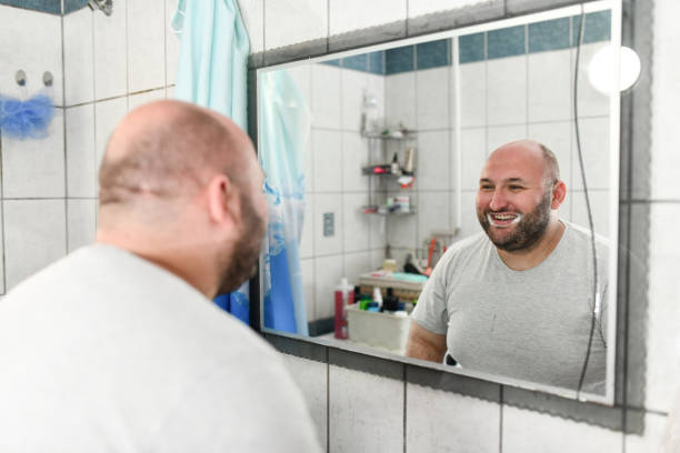 istock Overweight Male Practicing His Smile In Mirror While Washing Teeth 1498210763