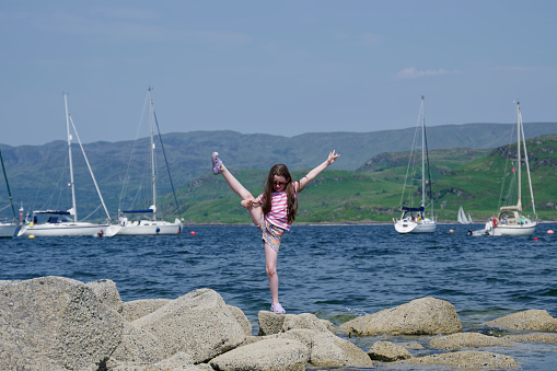 Young girl balancing doing a gymnastic move on rocks at Tighnabruaich in Argyll and Bute UK