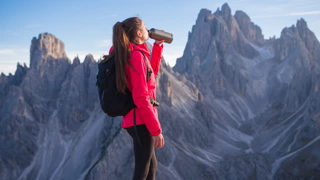 Woman adventurer taking a break and drinking water on mountain hike