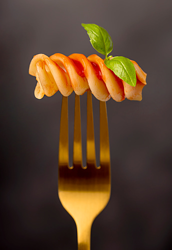 Macro food photography of giant fusilli, pasta, tomato, sauce; ketchup, basil, durum wheat semolina, fork, background