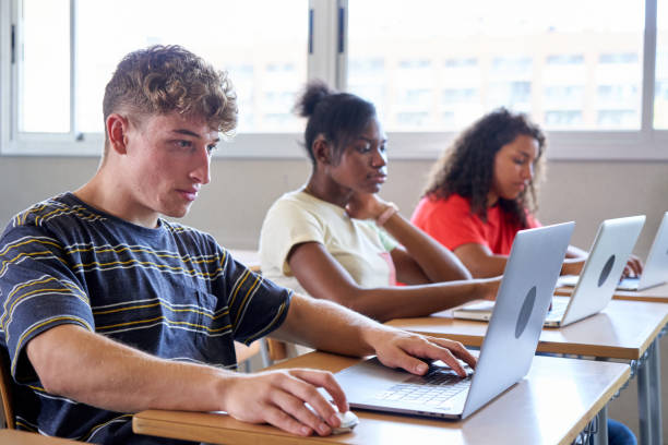 istock Side view of teenage students in a classroom studying with technological equipment, using laptops. 1498216966