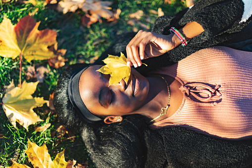 Young adult black woman lying down in yellow autumn leaves