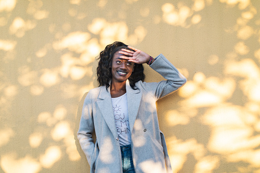 Young adult black woman portrait at yellow wall at sunset