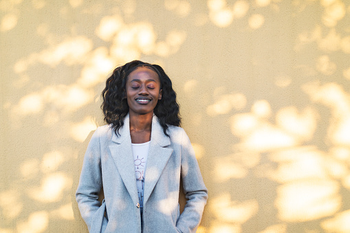 Young adult black woman portrait at yellow wall at sunset