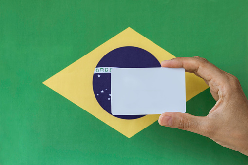 Hand holding blank card in front of flag of Brazil. Representing identity and citizenship concept.